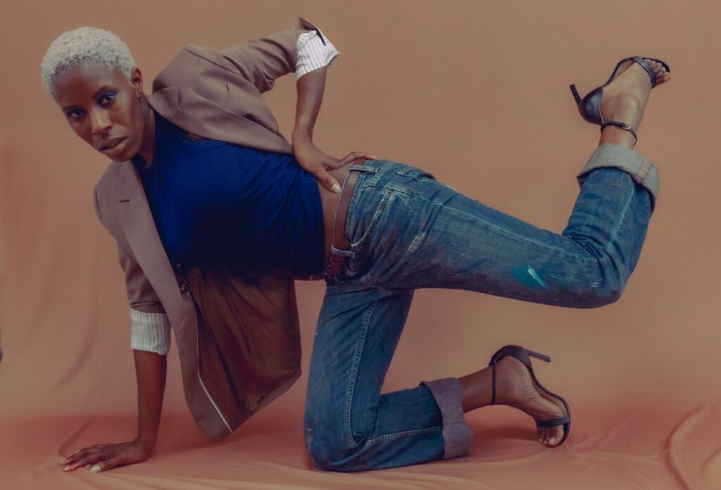 A stylish fashion model poses creatively in a suit jacket and jeans, emphasizing modern fashion trends.