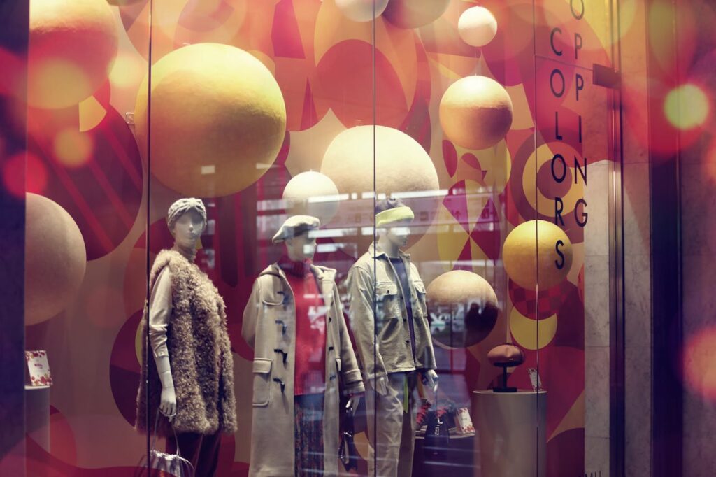 Stylish window display with trendy outfits on mannequins, vibrant design.